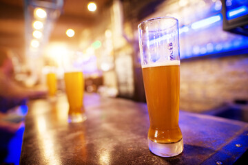 Close up view of draft beer glass placed on a bar table with a row of other in the background.