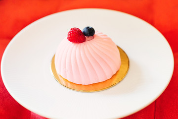 delicate pink mini cake on a large white plate. a plate of dessert on a soft red chair