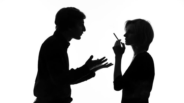Angry man shouting at his girlfriend smoking cigarette in front of him, quarrel