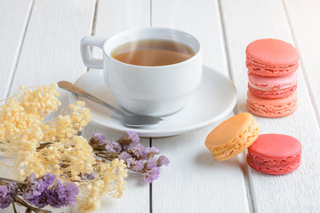 Different types color of macaroons with Cup of hot tea on white wooden background