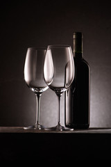 bottle of wine with two empty glasses on black