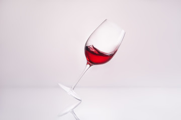 inclined wineglass with delicious red wine on reflective surface and on white