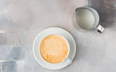 The cup of latte or cappuccino coffee with milk. Background with tools for making fresh boiled coffee: a glass of milk, coffee beans, a horn from a coffee machine.