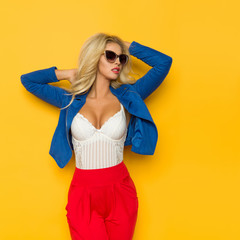 Beautiful Blond Woman In Blue Unbuttoned Jacket And Sunglasses Is Posing With Hands Behind Head