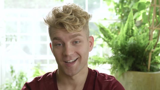 Young man with blonde hair shaking head towards camera.