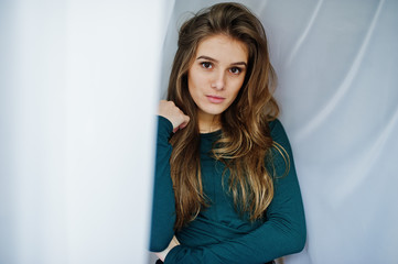Naklejka premium Handsome brunette girl wear on green, posing at curtains. Studio model portrait.