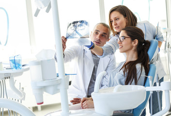 Dentist and his assistant in dental office talking with female patient and preparing for...