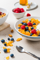 Healthy breakfast. Corn flakes with yogurt, almonds, blueberries, raspberries and chia seeds. Served with maple syrup and juice on beige fabric background.