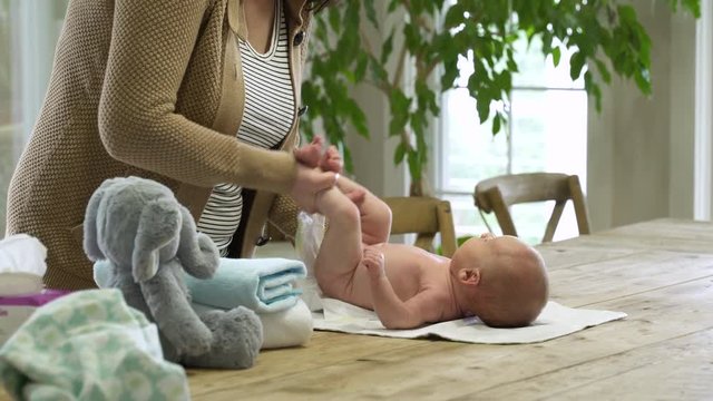 Mum changing newborn baby's nappy on wooden table.