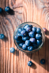 Freshly gathered blueberries put into jar. Some fruits scattered on old wooden table