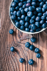 Freshly gathered blueberries put into bowl. Some fruits scattered on wooden old table