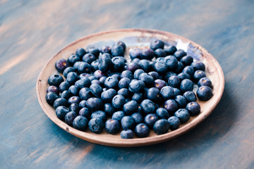 Freshly gathered blueberries put on plate. Table painted in blue in the background