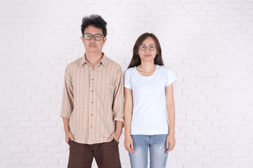 Stylish couple in casual clothes is looking at camera and smiling, against a background of a brick wall.