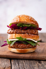 Homemade classic beef burger with double patty, cheese, lettuce, onion, tomato and sauce on a wooden background. Delicious food