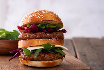 Homemade classic beef burger with double patty, cheese, lettuce, onion, tomato and sauce on a wooden background. Delicious food