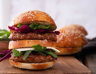 Homemade classic beef burger with double patty, cheese, lettuce, onion, tomato and sauce on a wooden background. Delicious food