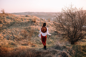 Beautiful girl with a map, binoculars and hat on top of the mountains walking at sunset. Soft focus. Back view
