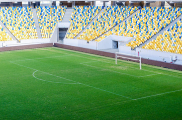 Fototapeta premium Siedzący kibice kolorowe plastikowe krzesła na tle stadionu piłkarskiego. Pusty stadion boisko do piłki nożnej zielona trawa na arenie lekkoatletycznej piłki nożnej.