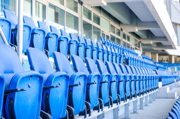 Obraz premium Siedzący kibice kolorowe plastikowe krzesła na tle stadionu piłkarskiego. Pusty stadion boisko do piłki nożnej zielona trawa na arenie lekkoatletycznej piłki nożnej.