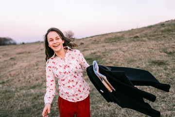 Stylish traveler woman with hat holding map on top of mountains, emotional happy moment, travel concept, space for text. Girl  walking along the grass at the top of the mountain in sunset