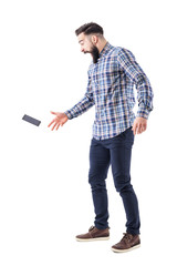 Screaming shocked young bearded man dropping mobile phone falling on the ground in mid air. Full body isolated on white background.  - obrazy, fototapety, plakaty