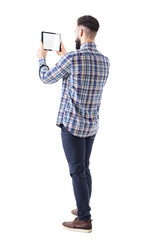 Side back view of young business bearded man holding pad tablet computer taking photo. Blank screen. Full body isolated on white background.  © sharplaninac