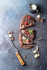 Sliced homemade sweet dessert chocolate pizza with different chocolates, raspberries and mint with knife and ingredients above over blue texture background. Top view, space.