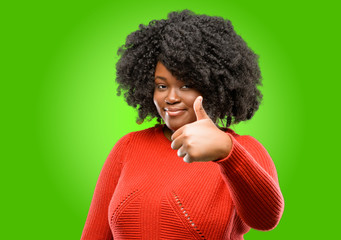 Fototapeta na wymiar Beautiful african woman smiling broadly showing thumbs up gesture to camera, expression of like and approval