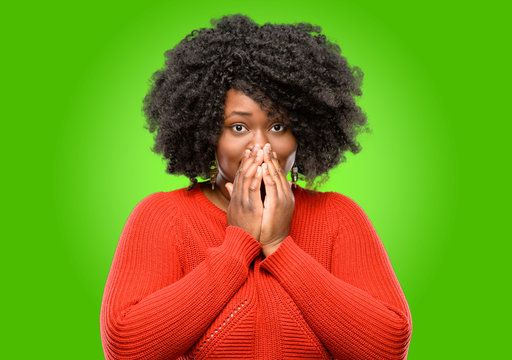Beautiful african woman covers mouth in shock, looks shy, expressing silence and mistake concepts, scared
