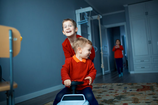 Two happy children riding on baby car in room, indoors.