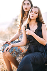 two beautiful girlfriends in summer dress with patterns of light walking and posing near the rocks at sunset