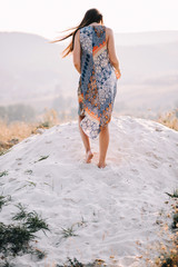 beautiful girl in summer dress with patterns of light walking and posing near the rocks on the sand...
