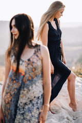 Obraz premium beautiful young girls walking in the light of long summer dresses for mountainous terrain, sand and posing. the wind and the sunset