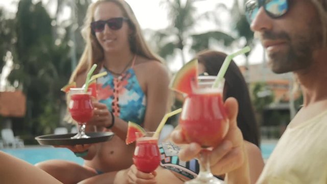 Summer pool party. Close up of fresh juice. Girl with a tray and glasses with smoothie. Happy group of young friends enjoying the natural drinks together in the resort. Healthy lifestyle.
