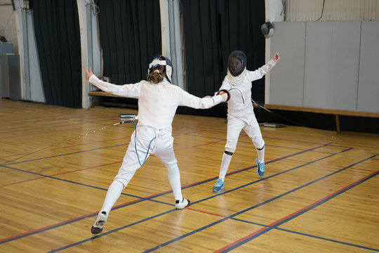 Girls, participants in fencing competitions are fighting on swords, epees. One girl is pricking another with a sword, epee