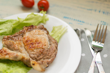 A piece of fried meat on a white plate on a light wooden background.