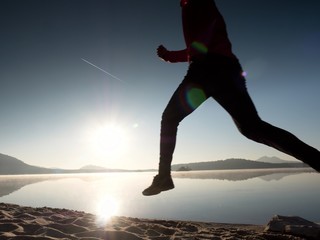 Man with sunglasses, red baseball cap and red black sportswear is running and exercising on beach.