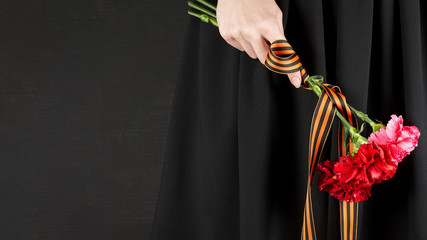 A woman holding a bouquet of red carnations with St. George ribbon at Victory Day celebrations