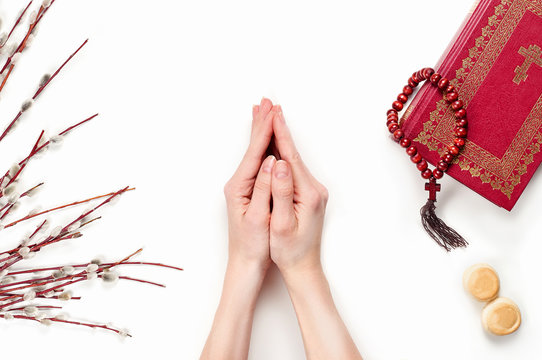 Female hands holding folded in prayer. The Still life with willow branches, liturgical bread, Bbible and rosary beads