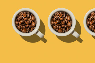 Cup concept. White cups with coffee beans on yellow background.  Creative style.