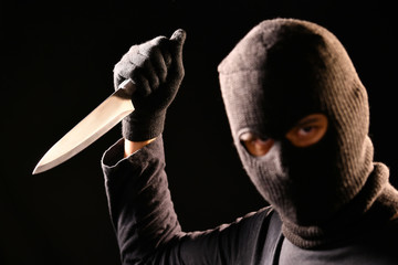 The robber hold the knife in hand on black background