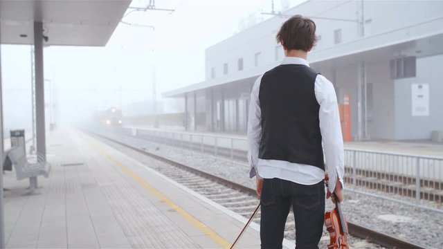 Violinist wait for train in early morning fog 4K