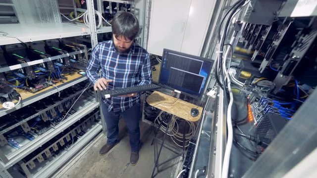 Mining rig with a male specialist in it controlling bitcoin mining process