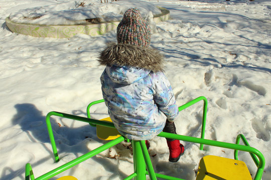 A little girl is sitting alone on a swing and is bored. A lonely child on the street.