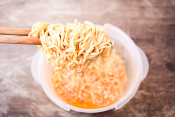 Hand uses chopsticks to pick up tasty noodles, instant noodles in a white cup and utensils ready to eat. Do not over mix something else (low class)