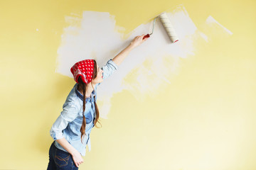 Beautiful girl in red Headband painting the wall with paint roller. Portrait of a young beautiful...