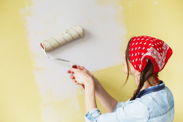 Beautiful girl in red Headband painting the wall with paint roller. Portrait of a young beautiful...