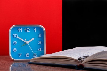 Blue alarm clock and opened personal organizer on red and black background