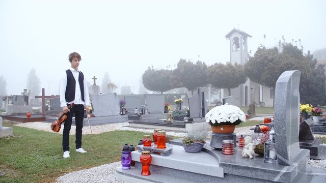 Boy with violin in hand stand infront a grave mourning 4K