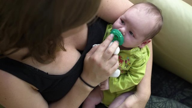 Mother nursing sleepy newborn daughter with dummy and soft toy.